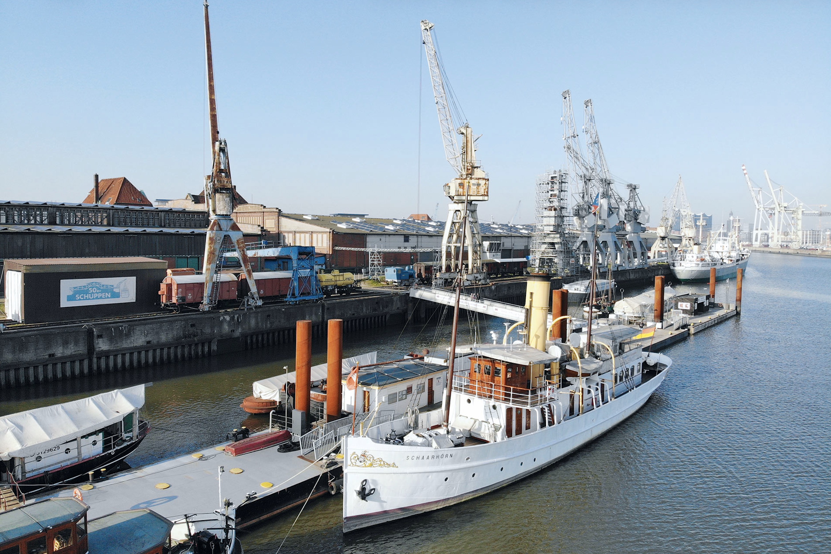 Im Vordergrund eine Pier, an beiden Seiten der Pier haben Schiffe angelegt. Im Hintergrund ein Kai.